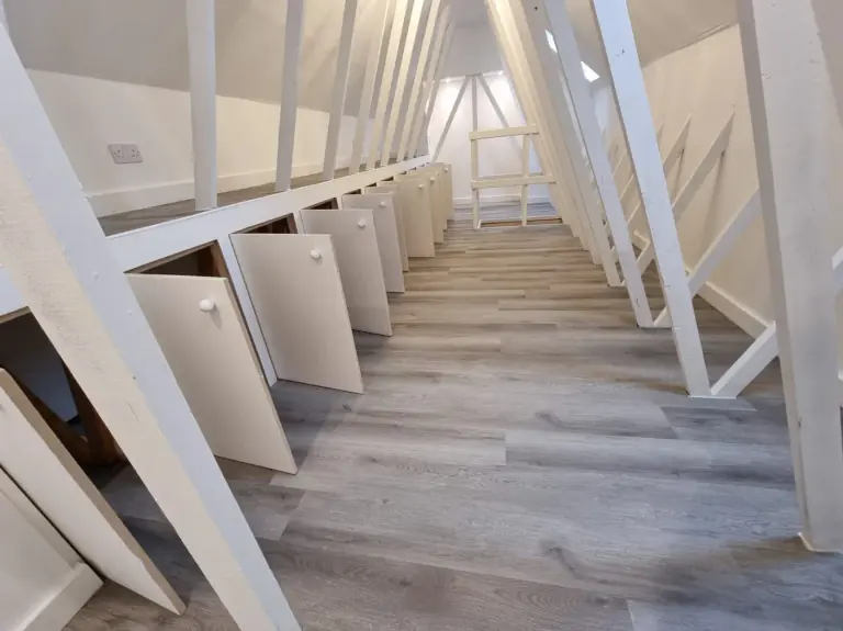 Premium loft storage room with handmade fitted cupboards, white-painted timbers and wood-effect flooring